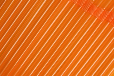 Many orange plastic drinking straws as background, closeup