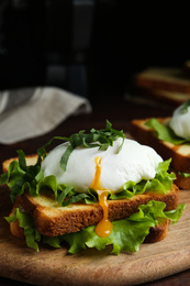 Photo of Delicious poached egg sandwich served on wooden board, closeup