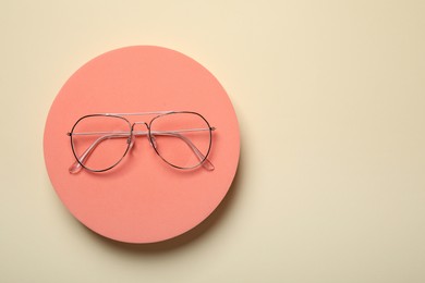 Stylish pair of glasses with metal frame on beige background, top view. Space for text