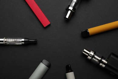 Many electronic smoking devices on black background, flat lay. Space for text