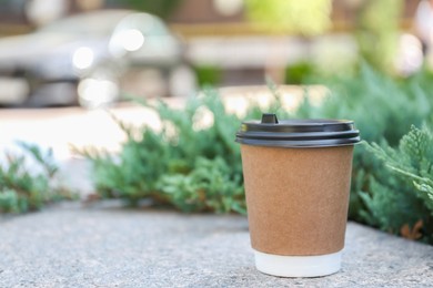 Photo of Disposable paper cup with plastic lid on stone parapet outdoors, space for text