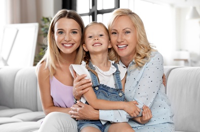 Photo of Young woman with mature mother and little daughter in living room