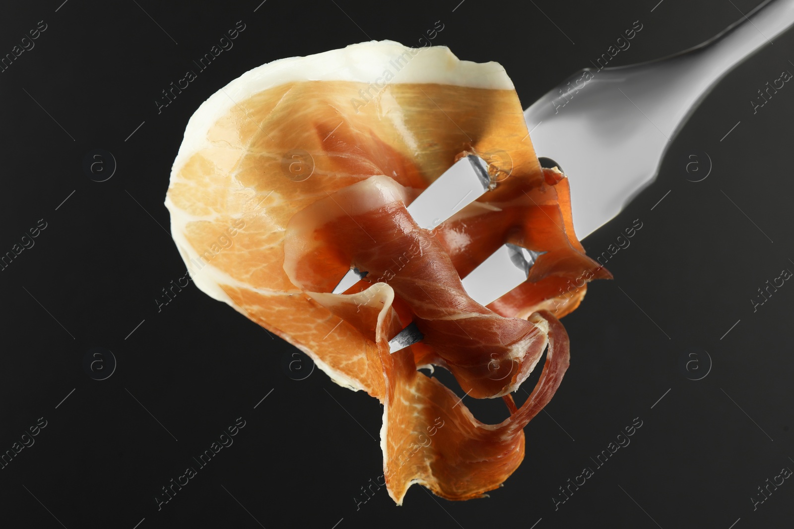 Photo of Fork with slice of tasty jamon on black background, closeup