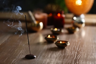 Photo of Incense stick smoldering on wooden table in room. Space for text