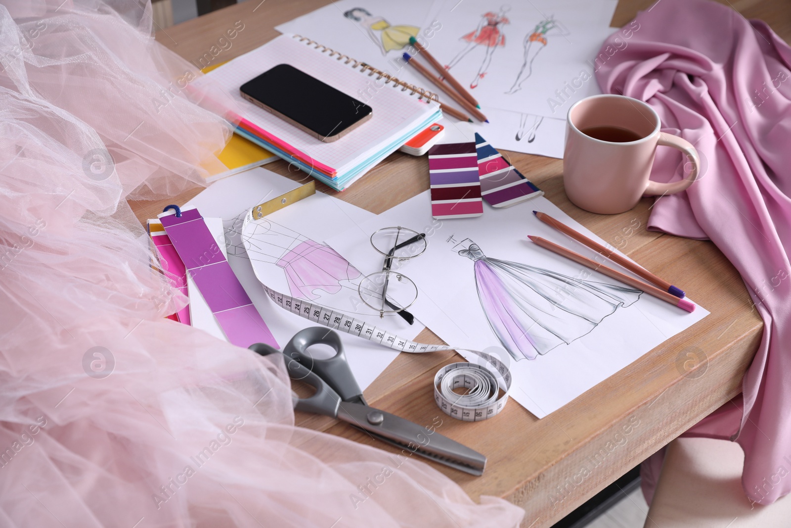 Photo of Sketches of clothes and different stuff on wooden table. Fashion designer's workplace