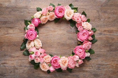 Photo of Wreath made of beautiful rose flowers and green leaves on wooden background, flat lay. Space for text