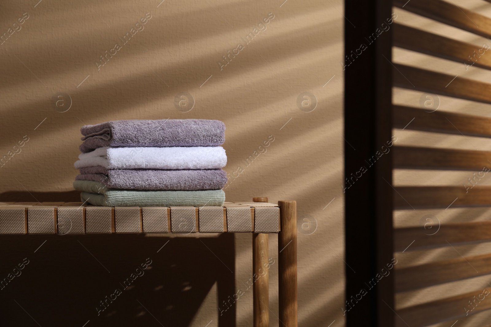 Photo of Stacked terry towels on wicker bench near beige wall, space for text