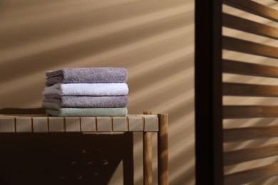 Stacked terry towels on wicker bench near beige wall, space for text