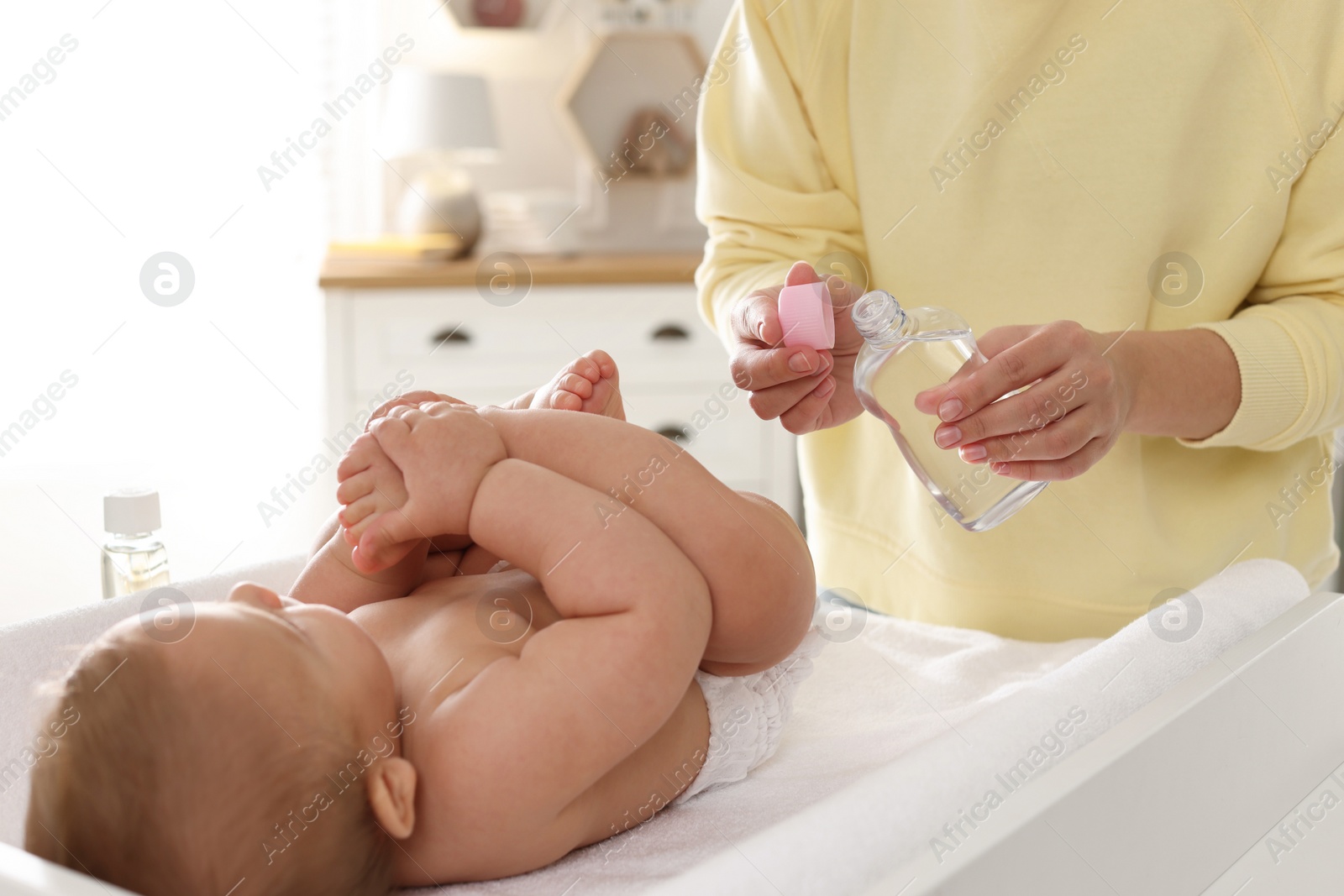 Photo of Mother with bottle of massage oil near baby on changing table at home, closeup