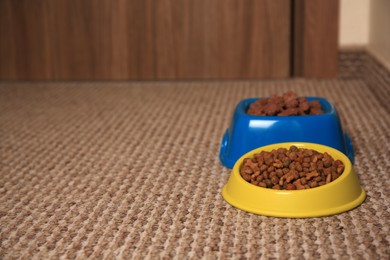 Photo of Dry and wet pet food in feeding bowls on soft carpet, space for text