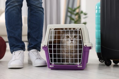 Photo of Travel with pet. Man near carrier with cute cat at home, closeup