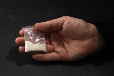 Photo of Drug addiction. Man with plastic bag of cocaine at grey table, closeup