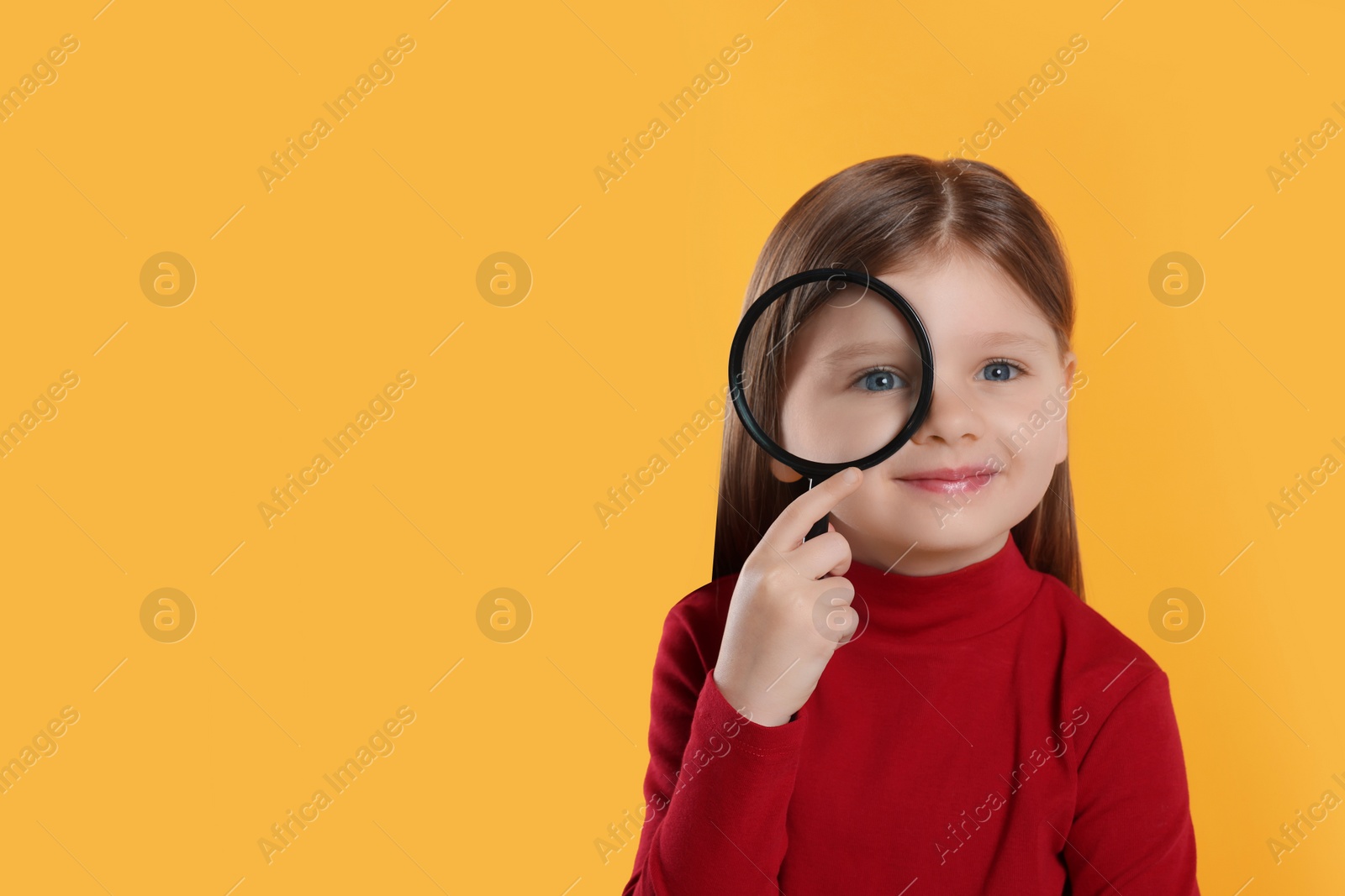 Photo of Cute little girl looking through magnifier on yellow background. Space for text