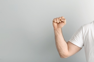 Young man showing clenched fist on light background. Space for text