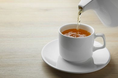 Photo of Pouring green tea into white cup with saucer on wooden table, closeup. Space for text