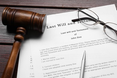 Photo of Last Will and Testament, glasses, pen and gavel on wooden table, closeup