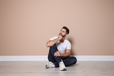 Young man sitting on floor near beige wall indoors