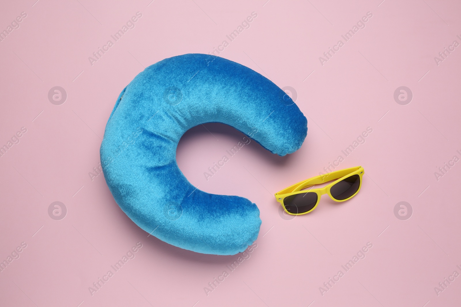 Photo of Light blue travel pillow and sunglasses on pink background, flat lay