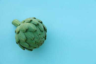 Whole fresh raw artichoke on light blue background, top view. Space for text