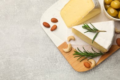 Photo of Pieces of tasty camembert cheese, rosemary, nuts and olives on grey textured table, top view. Space for text