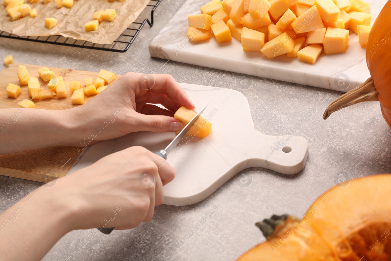 Photo of Woman cutting fresh pumpkin at light grey table, closeup