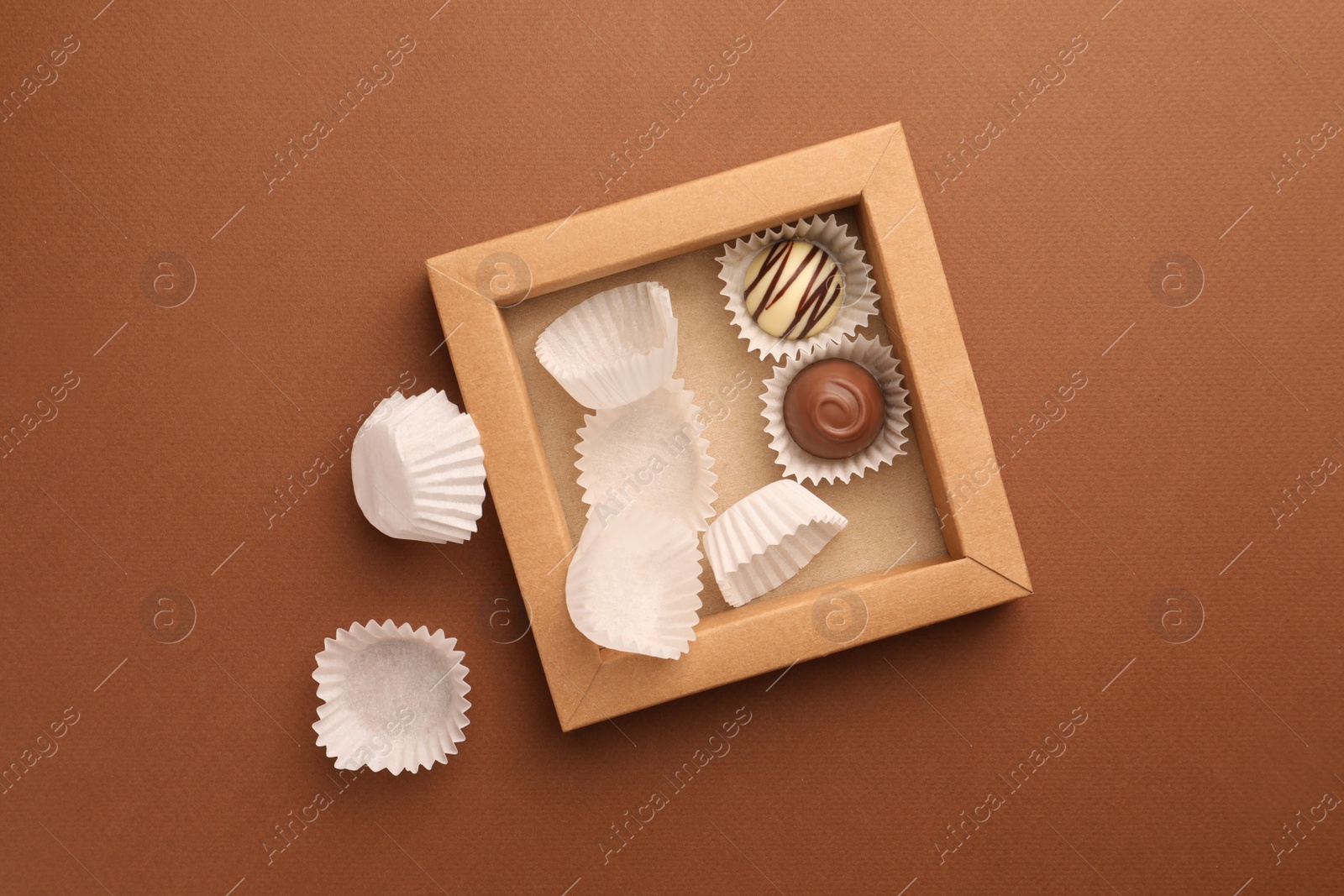 Photo of Partially empty box of chocolate candies on brown background, top view
