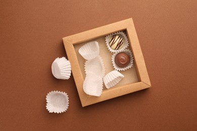 Photo of Partially empty box of chocolate candies on brown background, top view