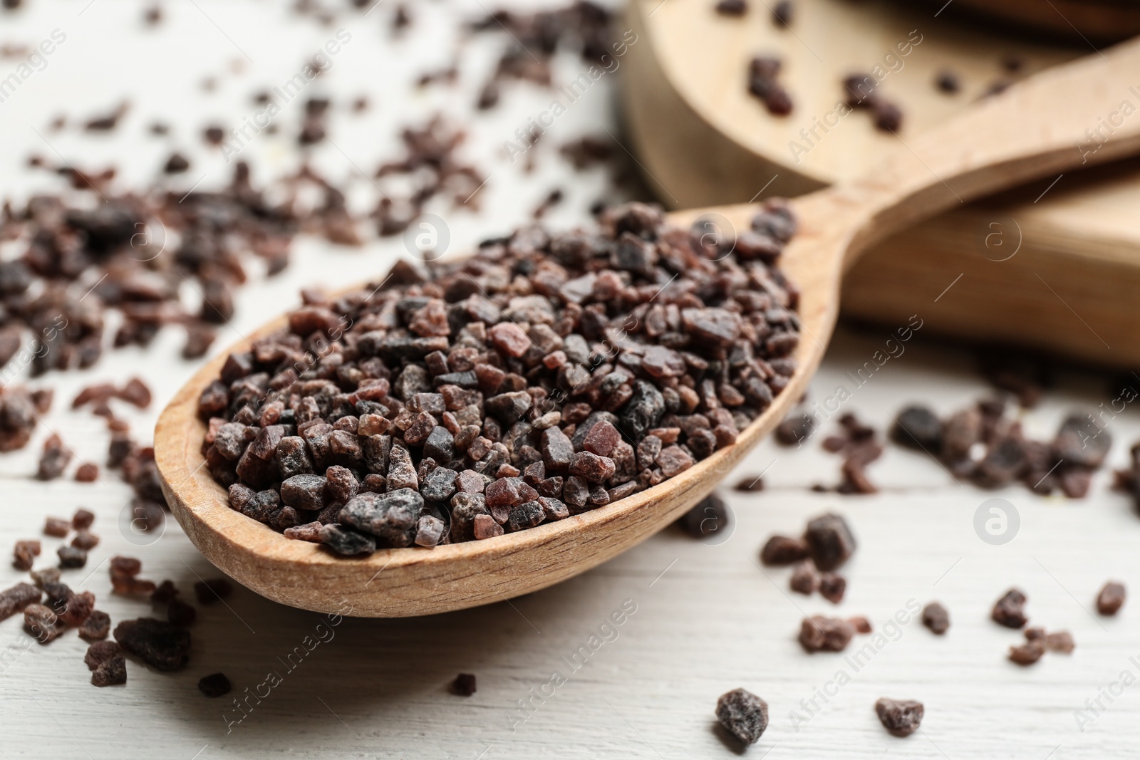 Photo of Spoon with black salt on white wooden table, closeup