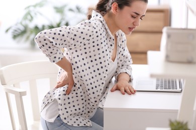 Photo of Woman suffering from back pain in office. Bad posture problem
