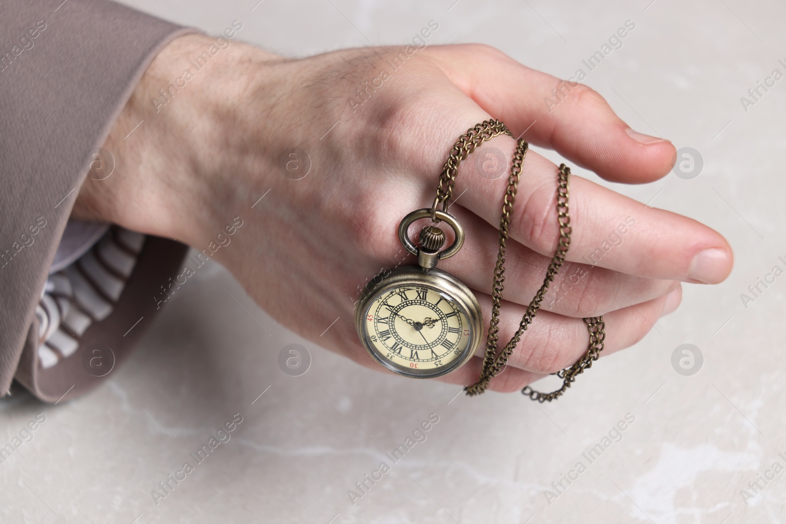 Photo of Man holding chain with elegant pocket watch at light marble table, closeup