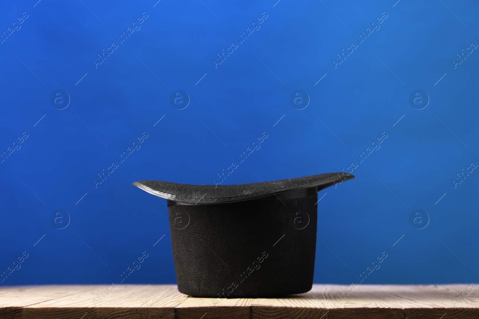 Photo of Magician's hat on wooden table against blue background, space for text