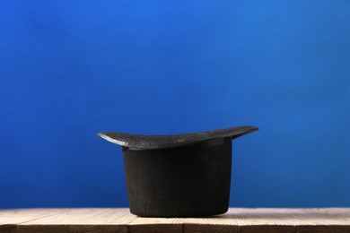 Photo of Magician's hat on wooden table against blue background, space for text