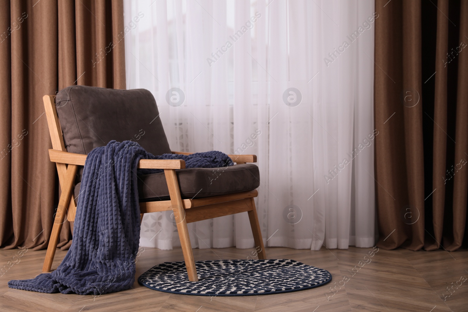 Photo of Comfortable armchair with blanket near window indoors, space for text. Interior design