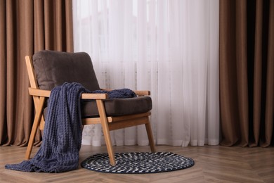 Photo of Comfortable armchair with blanket near window indoors, space for text. Interior design