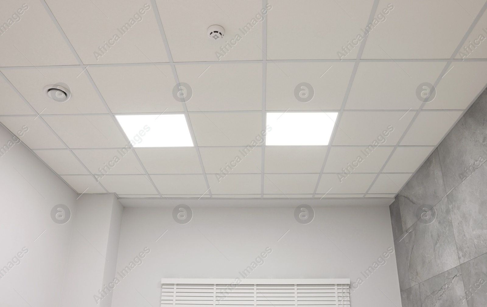 Photo of White ceiling with PVC tiles and lighting indoors, low angle view