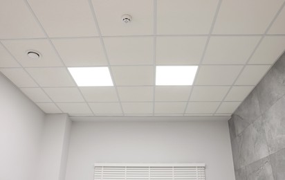 Photo of White ceiling with PVC tiles and lighting indoors, low angle view