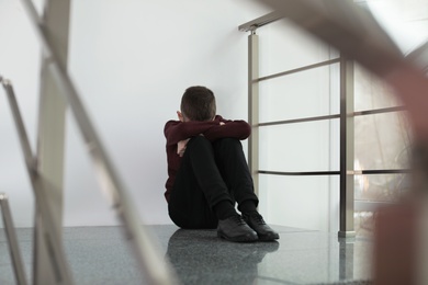 Upset preteen boy sitting on staircase indoors