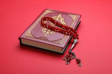 Photo of Muslim prayer beads and Quran on red background