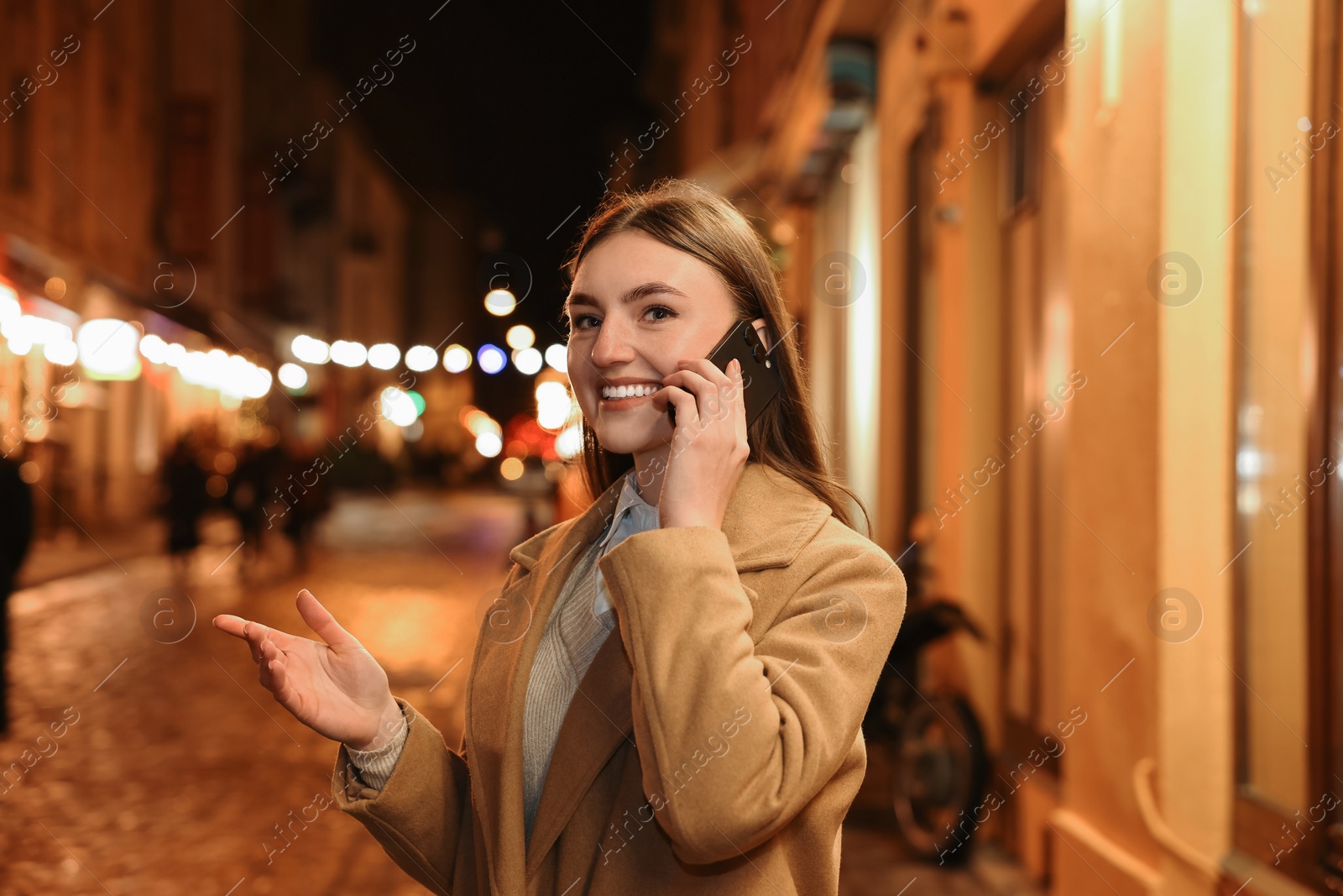 Photo of Smiling woman talking by smartphone on night city street