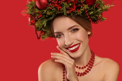 Photo of Beautiful young woman wearing Christmas wreath on red background, closeup