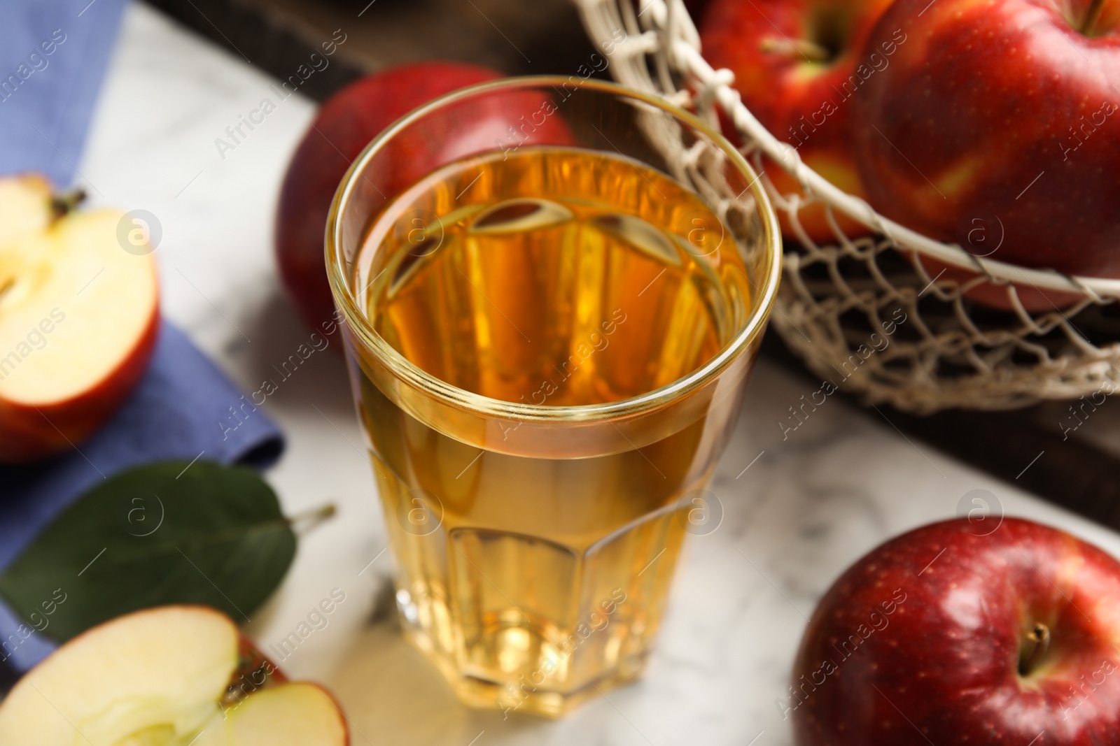Photo of Glass of delicious cider and ripe red apples on white marble table, closeup