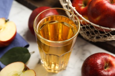 Photo of Glass of delicious cider and ripe red apples on white marble table, closeup