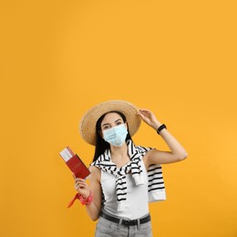 Female tourist in medical mask with ticket and passport on yellow background. Travelling during coronavirus pandemic