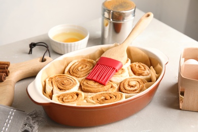Photo of Baking dish with raw cinnamon rolls and pastry brush on table