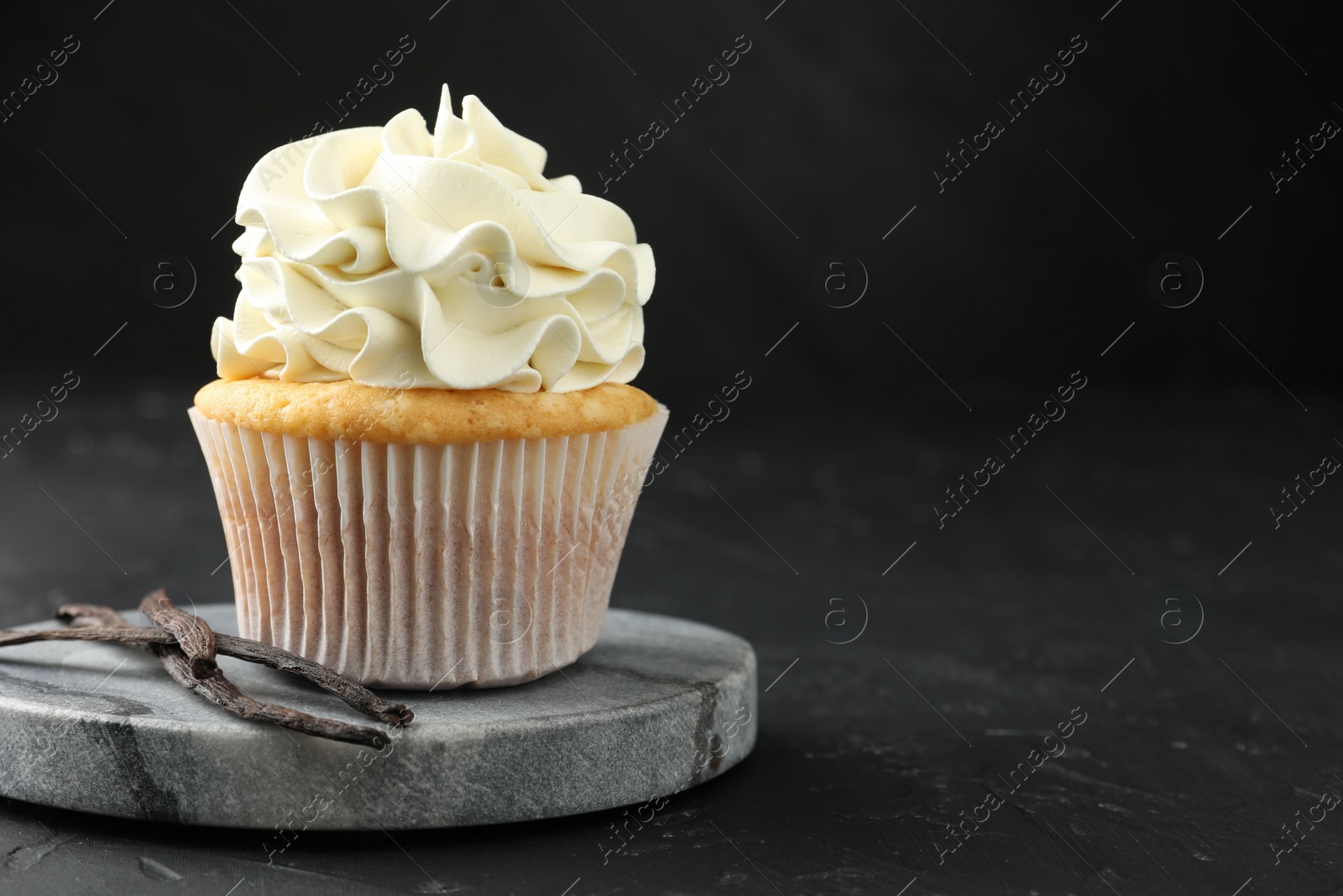 Photo of Tasty cupcake with cream and vanilla pods on black table, closeup. Space for text