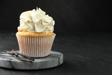 Tasty cupcake with cream and vanilla pods on black table, closeup. Space for text