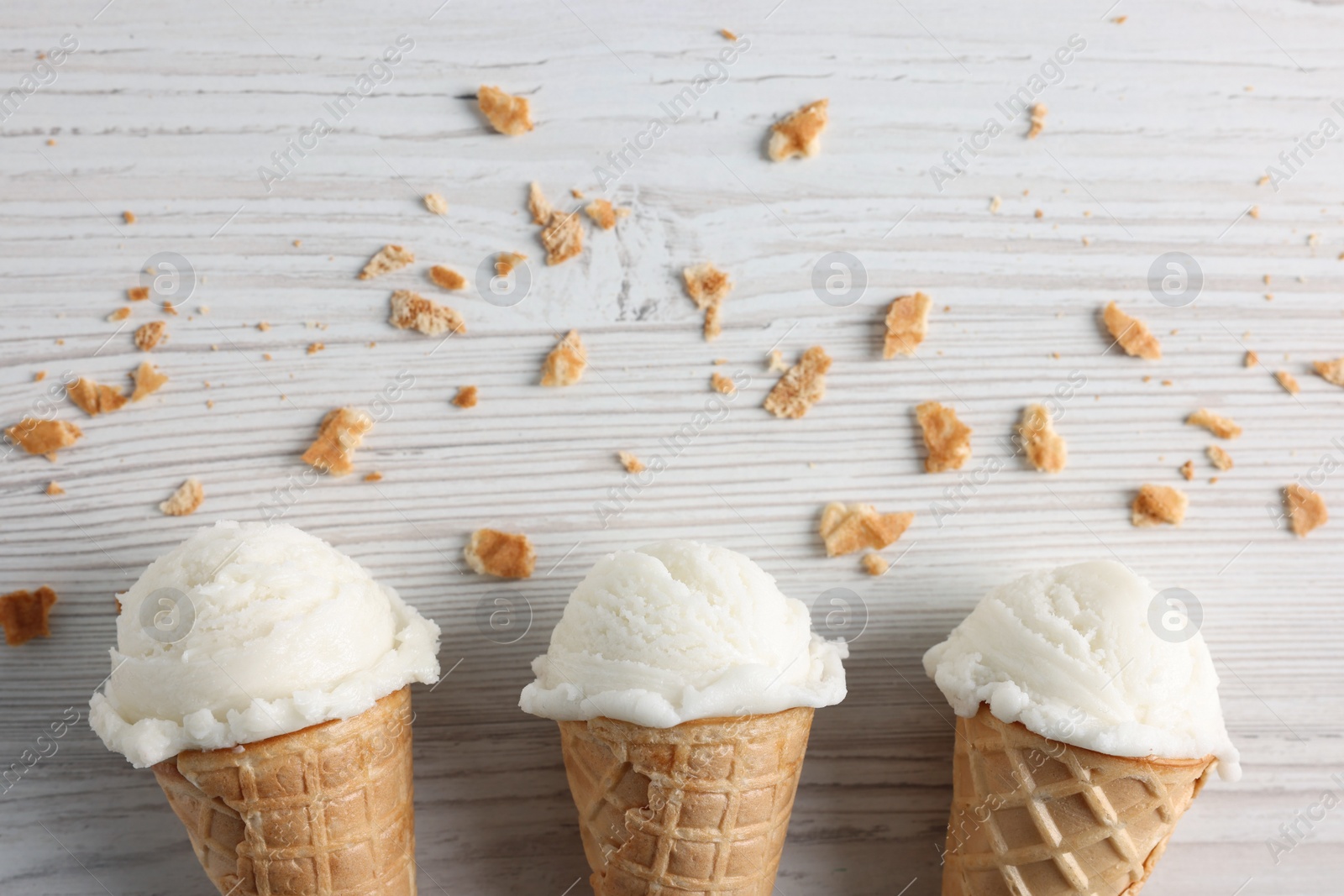 Photo of Ice cream scoops in wafer cones on light wooden table, flat lay