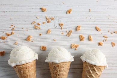 Photo of Ice cream scoops in wafer cones on light wooden table, flat lay