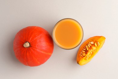 Photo of Tasty pumpkin juice in glass, whole and cut pumpkins on light background, flat lay