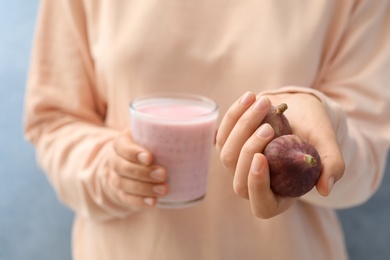 Woman holding smoothie and fresh figs on light blue background, closeup